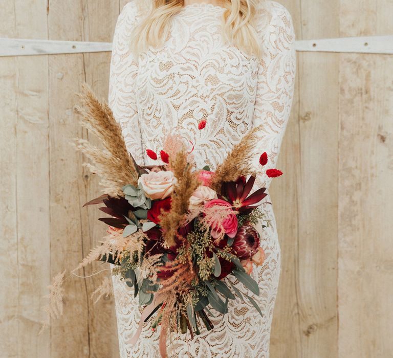 Bride in a high neck long sleeve lace wedding dress with a pink and red wedding bouquet 