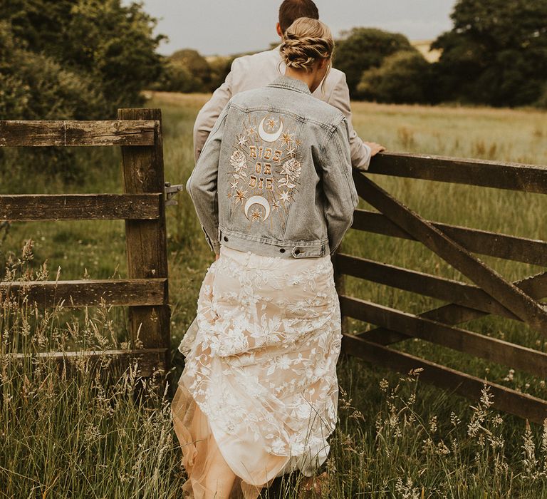 Bride in a light blue denim jacket with a cool design on the back for rustic wedding 