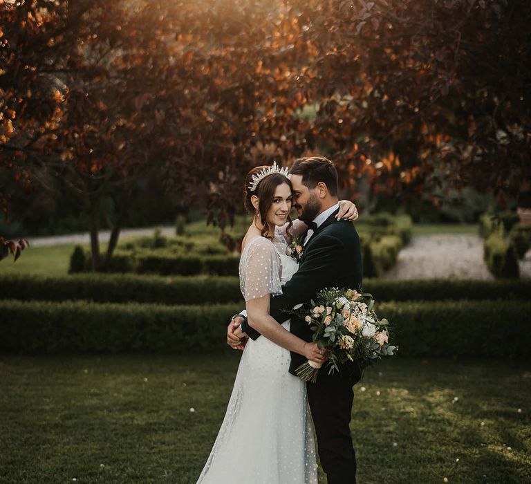 Golden hour strikes as the groom embraces the bride and she looks at the camera wearing a quartz crystal crown