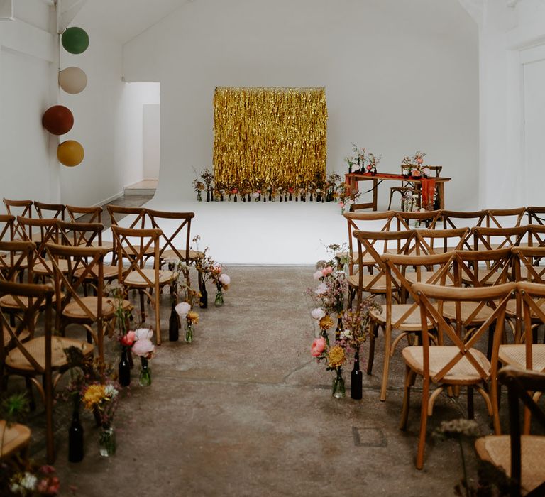 Gold streamers wedding decor for industrial styled wedding with wooden chairs and small floral arrangements lining the aisle