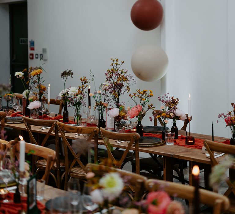 Retro coloured balloons and wooden banquet tables finished with orange table runner and small floral arrangement centrepieces 