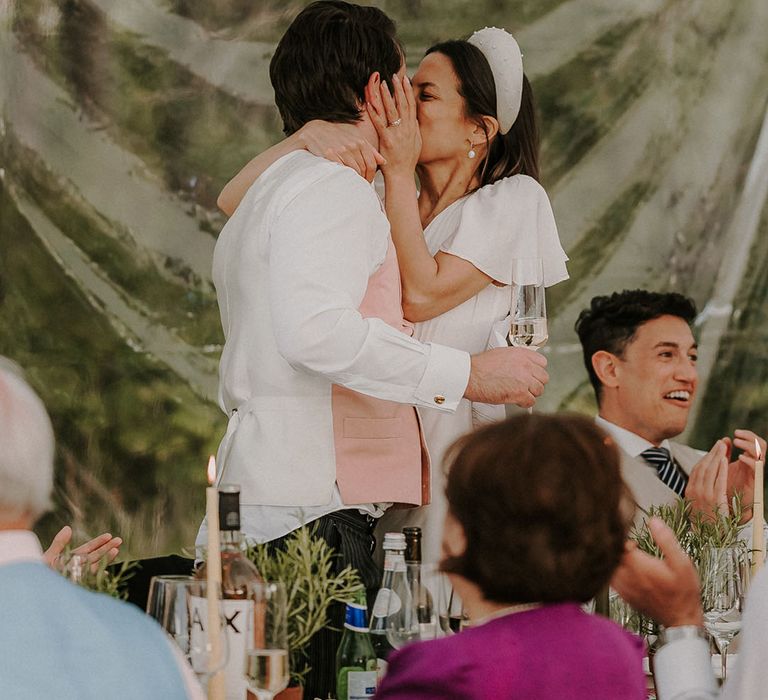 Bride and groom share a kiss as they stand at their marquee wedding reception 