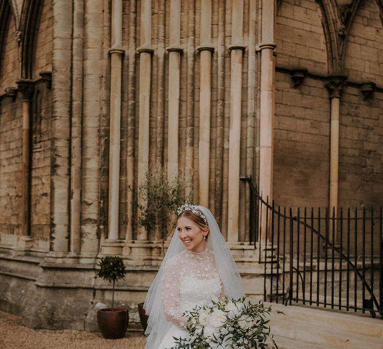 Bride in a lace high neck long sleeve lace A-line wedding dress with a flower headband and white flower bouquet 