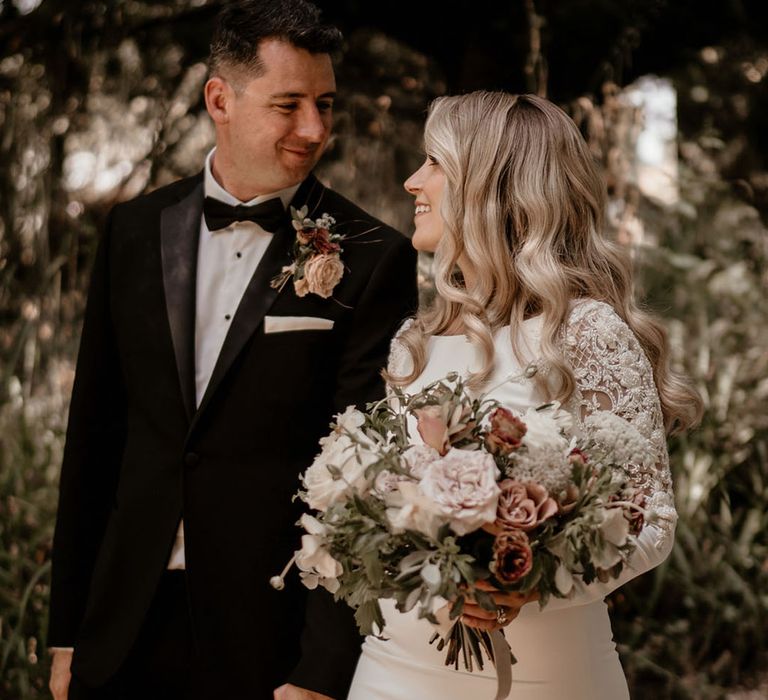 Groom in black tie with a pink buttonhole with the bride in a fitted long sleeve Badgley Mischka wedding dress for their classic wedding 