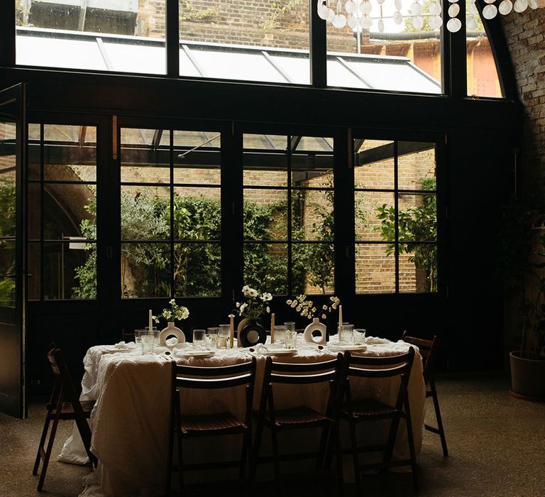 Minimalistic monochrome wedding tablescape with white tablecloth, black and white table decor, white floral arrangements underneath large alternative chandelier at golden hour