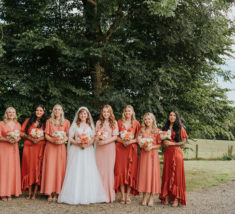 Bridal party in coral peach bridesmaid dresses standing with the bride in a lace and tulle wedding dress with a pink and white bouquet