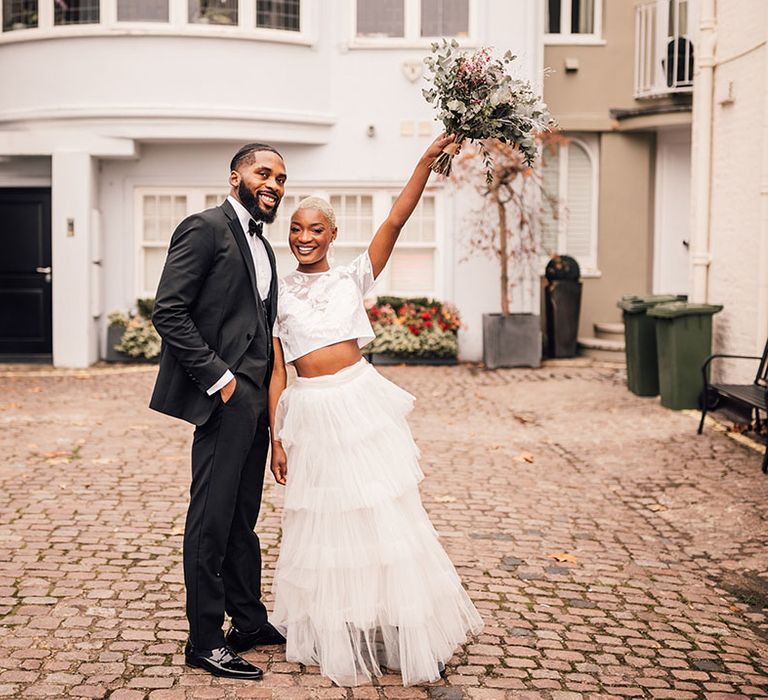 Bride holds bridal bouquet in the air in London mews with Groom