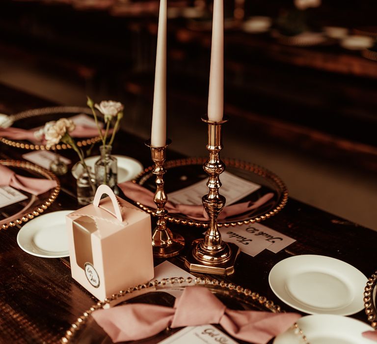 Rose gold candlestick holders on luxe wedding tablescape with rose gold plates, white rose floral decor and retro style wedding seat names