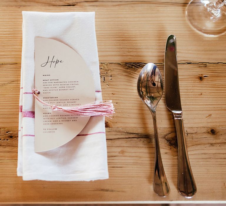 Crescent shaped off-white wedding dinner menu with baby pink tassel on white napkin with baby pink embroidery 