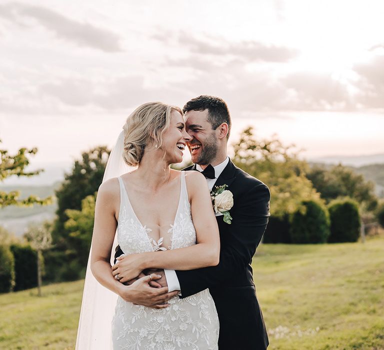 Groom in black-tie embraces his bride in plunge lace wedding dress