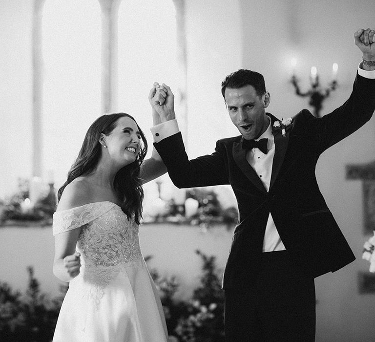 The bride and groom turn and face their wedding guests as they raise their arms in celebration 