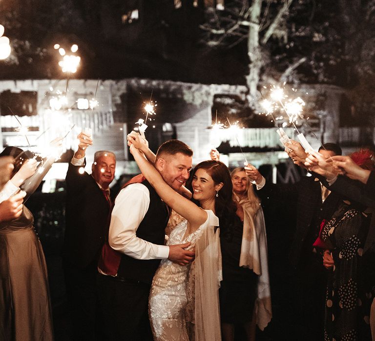 The bride and groom embrace each other as sparklers are wave around for their sparkler send off 