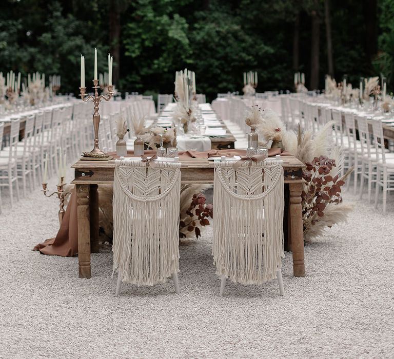 Macrame chair decor complete with wooden banquet tables with neutral colour scheme for outdoor destination wedding reception 