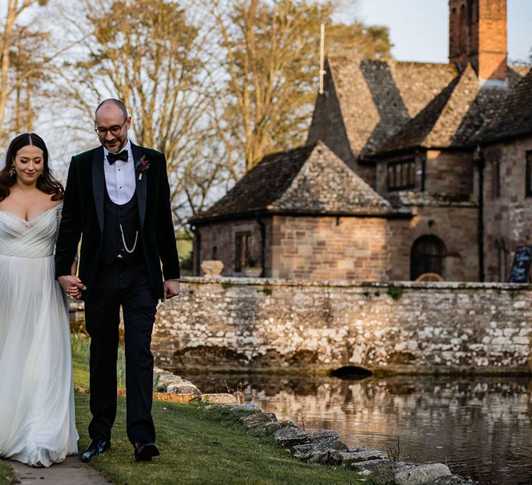 The bride in a tulle wedding dress and groom in a velvet tux walk around the grounds at Brinsop Court Manor House and Barn