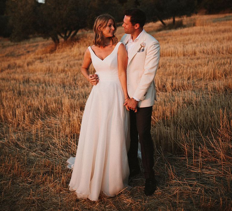 Bride in chic Suzanne Neville wedding dress leans into her groom during golden hour portraits in Italy