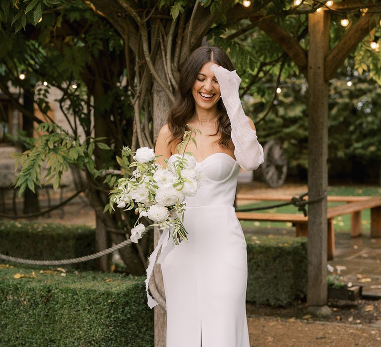 Bride in Bon Bride wedding dress with detachable pearl sleeves and Jimmy Choo pearl shoes with all white flower bouquet 