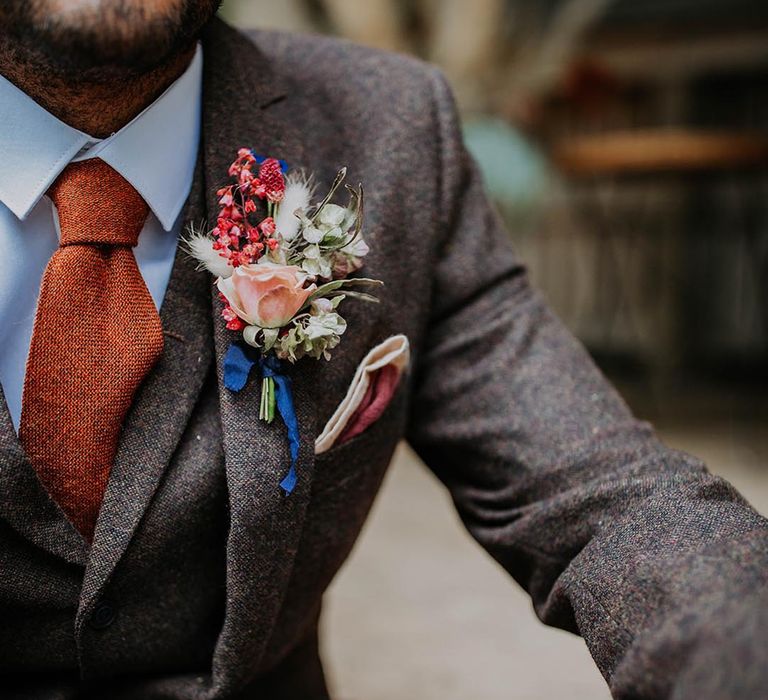 Groom in three piece grey suit with an orange tie with a pink and white buttonhole groom accessory 