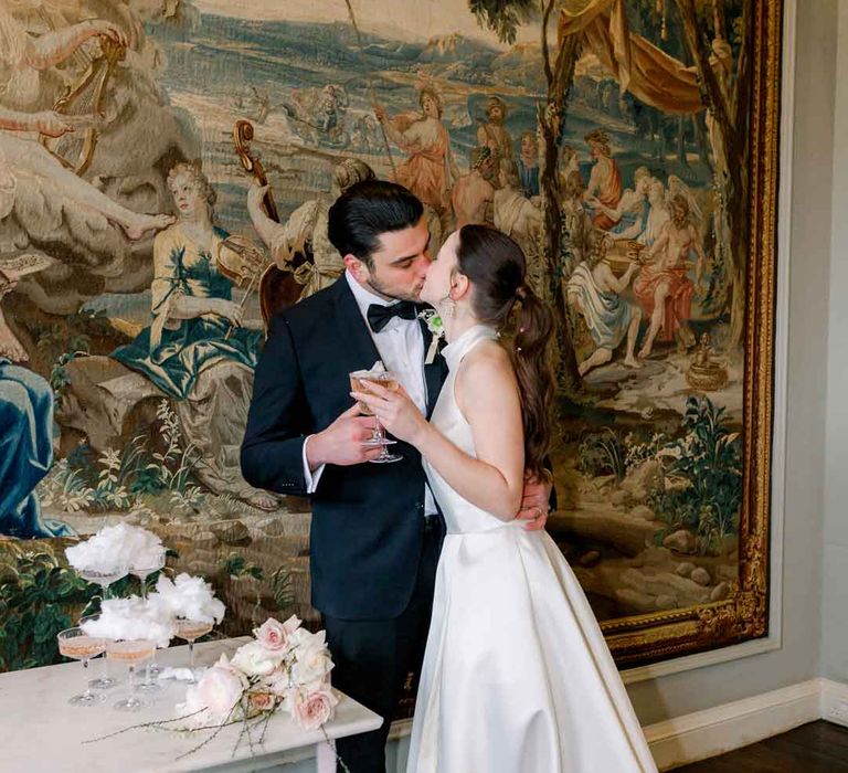 Bride in satin look halterneck wedding dress standing with groom in classic black tuxedo next to champagne tower with candy floss topper 