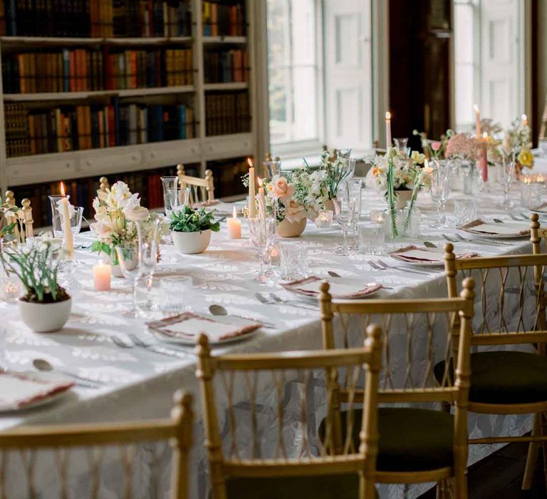 Classic wedding tablescape with white table cloth, pink tapered candles, spring florals and neutral toned napkins in the reception room of St Giles House 