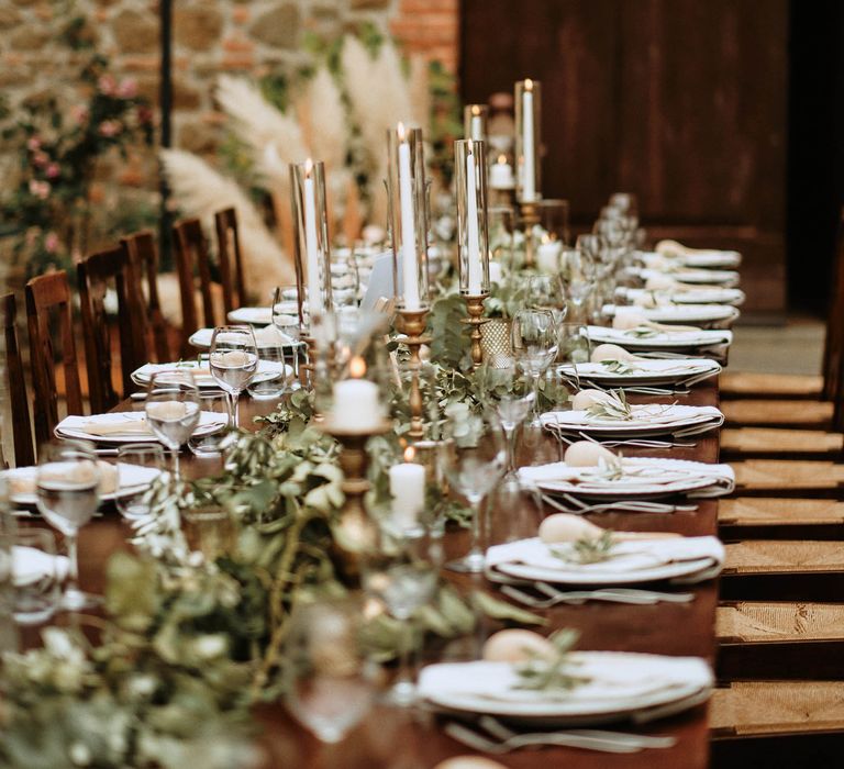 Wedding tablescape featuring eucalyptus decor with tapered candles, wine glasses and maraca favours