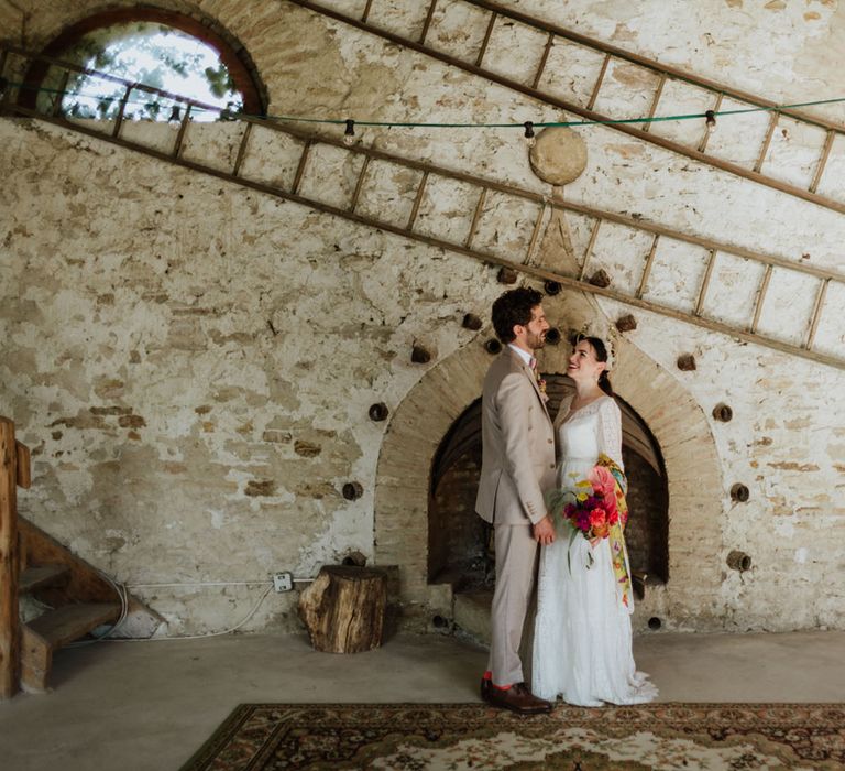 Bride and groom at rustic wedding venue in italy wearing a white lace wedding dress, boho bridal crown, and greige groom's suit