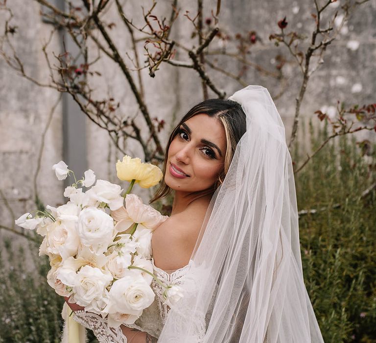 Bride in sequin long sleeve off the shoulder wedding dress holding white and pastel yellow bouquet with giant poppies 