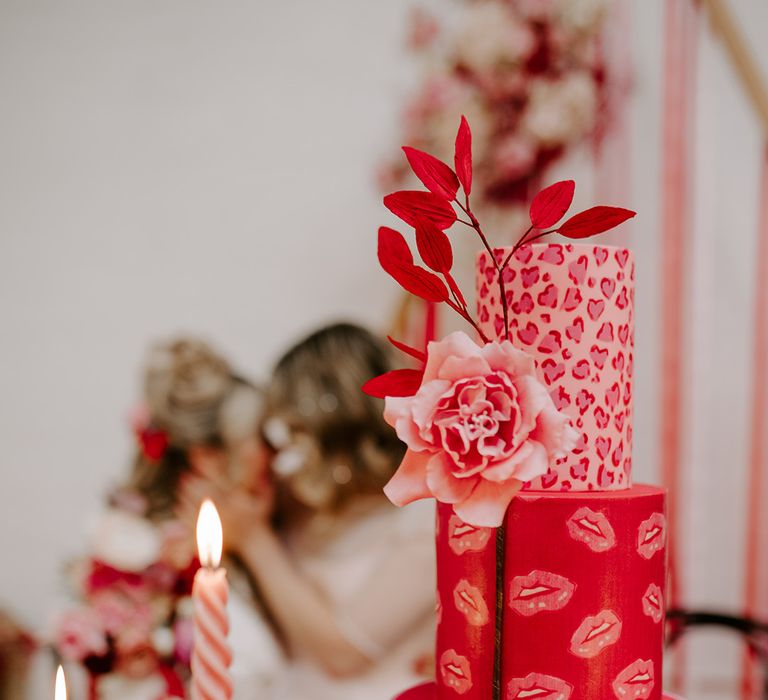 Three tier red and pink wedding cake with leopard prints, lip prints and colourful decor and candles for pink wedding theme 