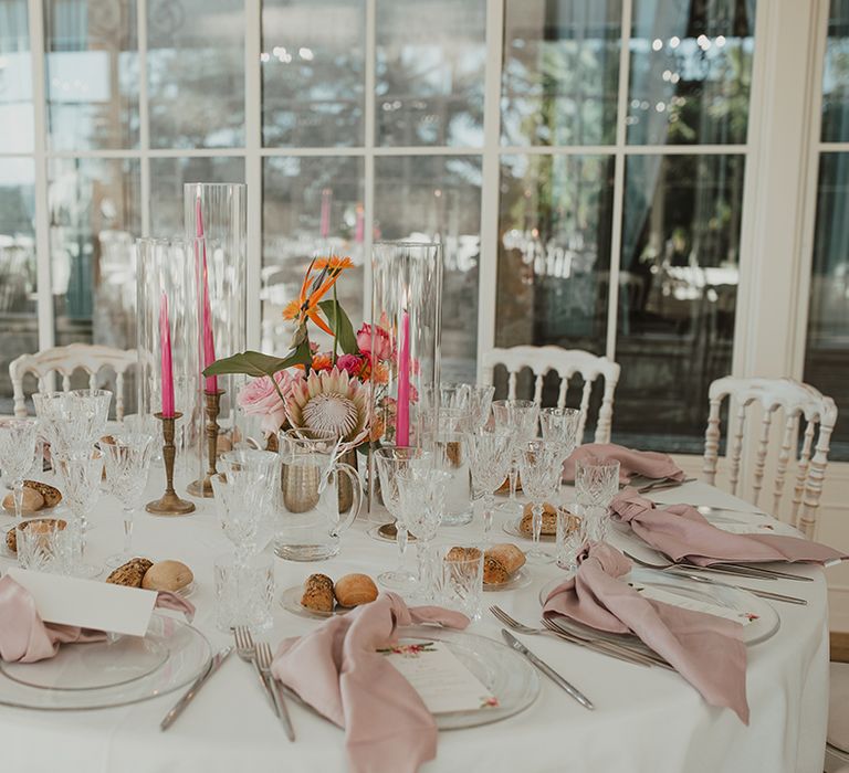 round wedding reception table with pink napkins and candles and tropical flower centrepiece