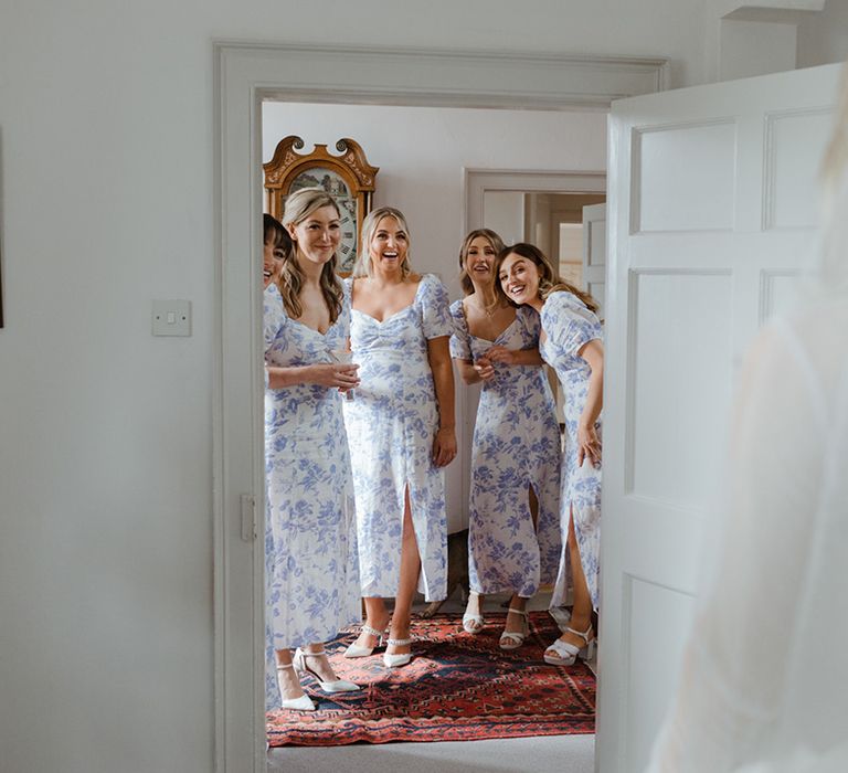 Bridesmaids in blue and white floral patterned bridesmaid dresses looking at the bride in her dress for the first time 