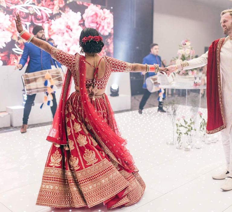 Bride in red and gold lehenga doing first wedding dance with groom in white and gold sherwani 