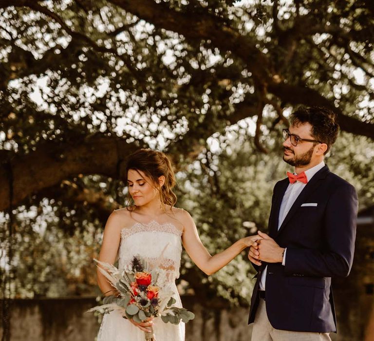 groom in grey chinos and navy blazer holding hands with his bride in a strapless lace wedding dress at greece destination wedding