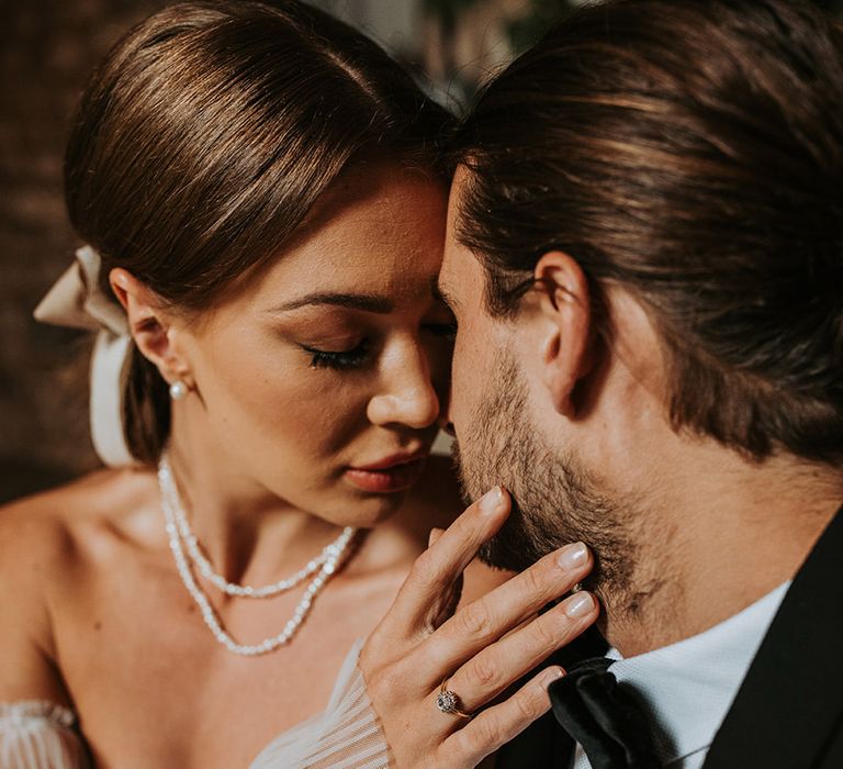 Groom in black tie leans in for a kiss with the bride in a corset style wedding dress with pearl jewellery at Eden Barn