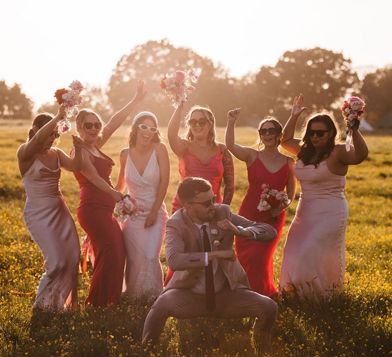 Bridesmaids in mismatched pink satin dresses with groom in taupe suit dancing in front of them 