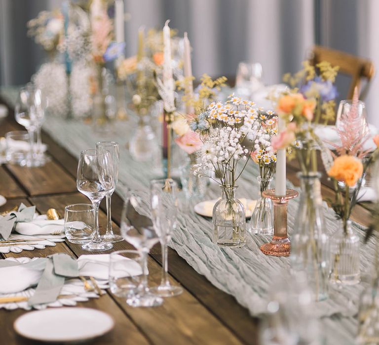 Pastel wedding theme tablescape with colourful bud vases, flowers, candles, and more at industrial style venue 