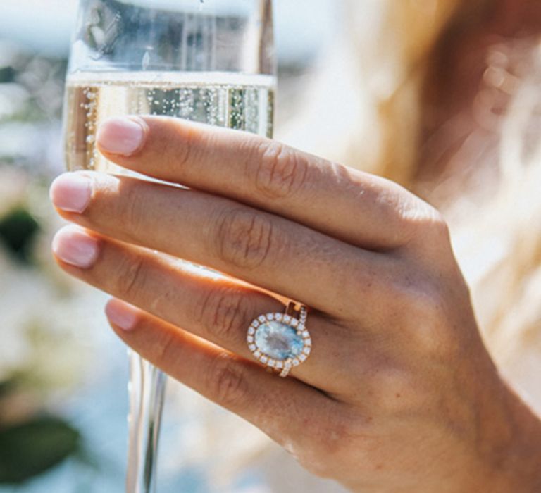 Bride wearing large light blue engagement ring with halo drinking champagne