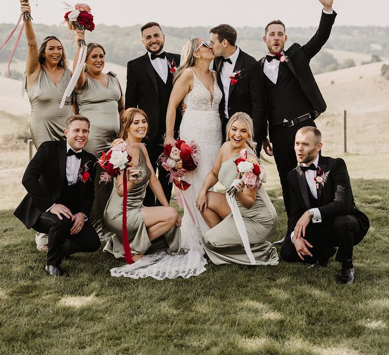 Group wedding photo with pink and red wedding theme with the bridesmaids wearing green satin bridesmaid dresses 