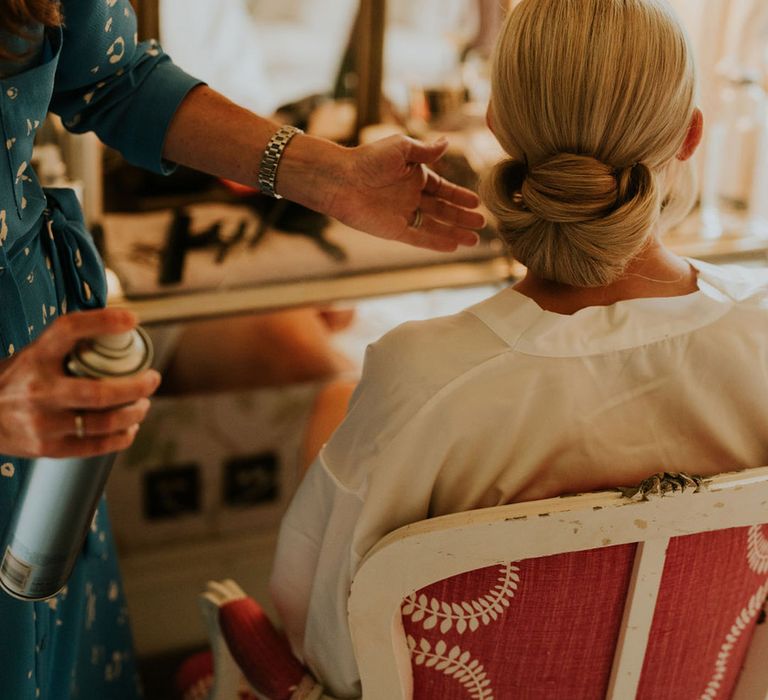 The bride gets her hair done for the wedding day in a sleek updo 