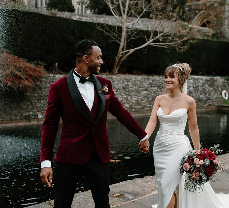 Bride in strapless wedding dress with sparkly Jimmy Choo wedding shoes with the groom in a red velvet suit jacket for their couple portraits