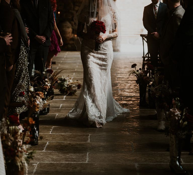 Bride walking down the aisle by herself with traditional veil and red rose bouquet 