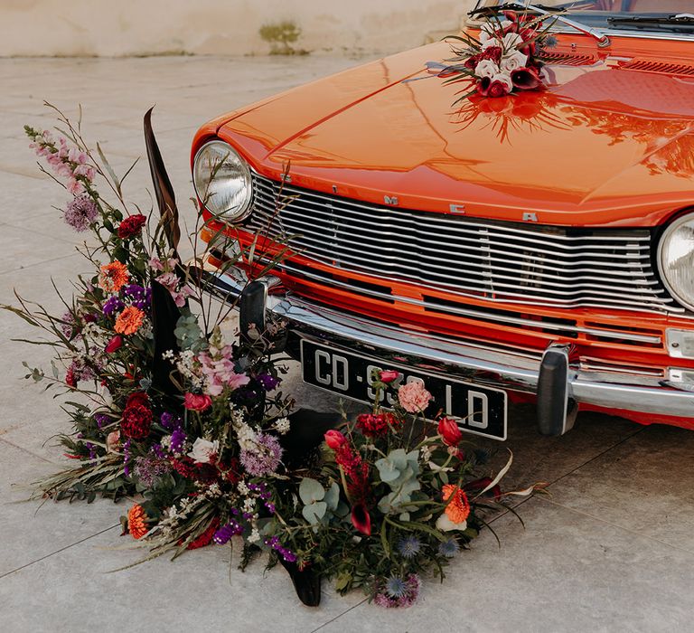 Red vintage wedding car decorated with red, purple and pink wedding flowers arrangements 