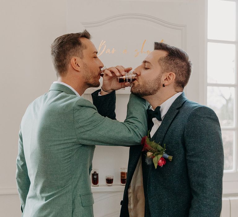 Grooms take a shot together at their wedding breakfast as they toast to their wedding 