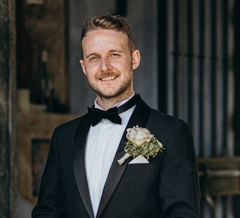 Groom in black tuxedo with a white rose buttonhole accessory 