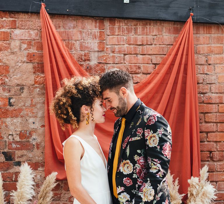 Stylish bride in wedding jumpsuit and groom in floral jacket 