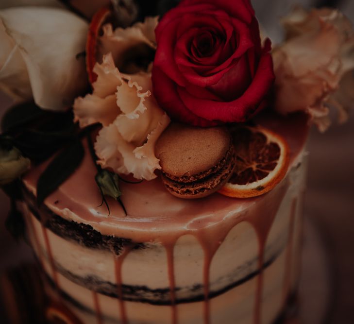 Naked wedding cake featuring drip effect with roses and macarons