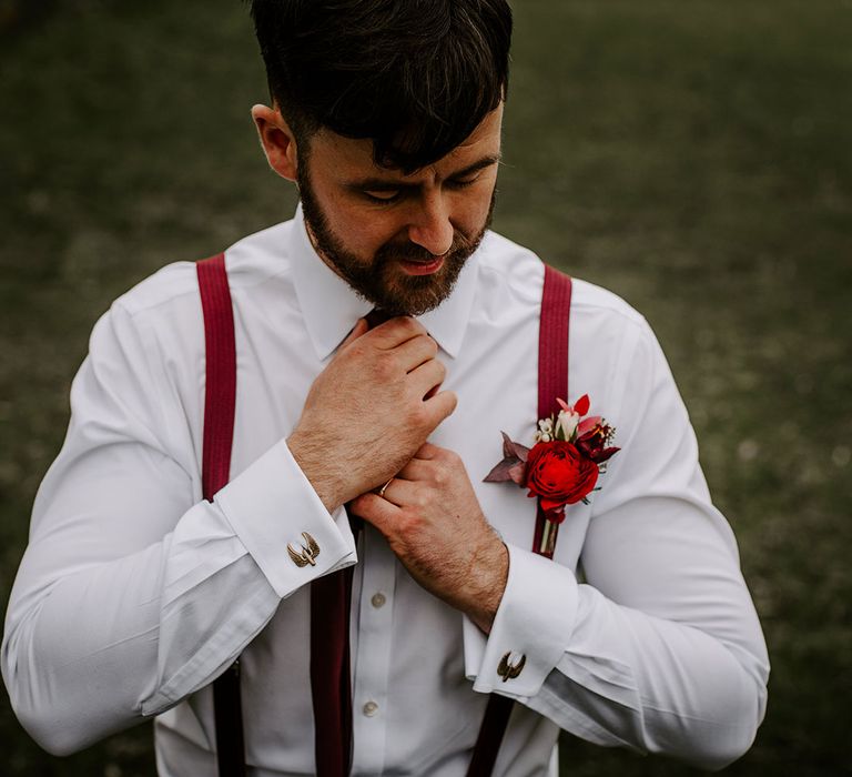 Groom with red braces adjusting red tie