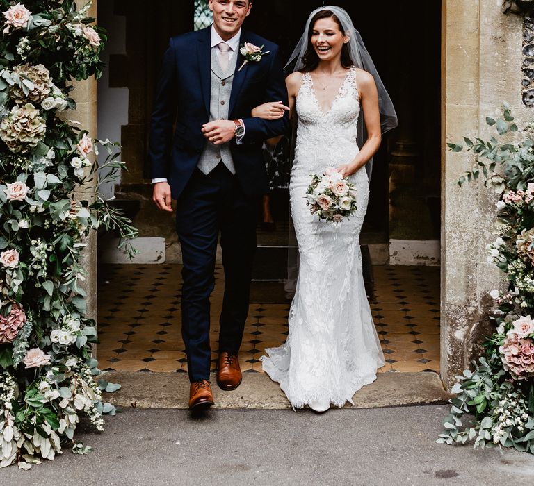 Bride & groom walking out of church with florals 