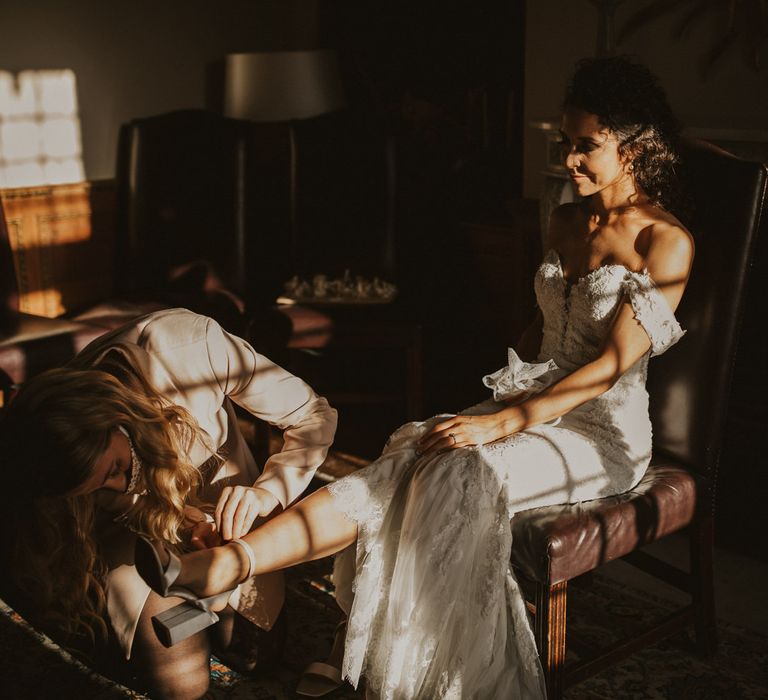 Bride on the wedding morning in a lace wedding dress putting on her strappy sandal wedding shoes 