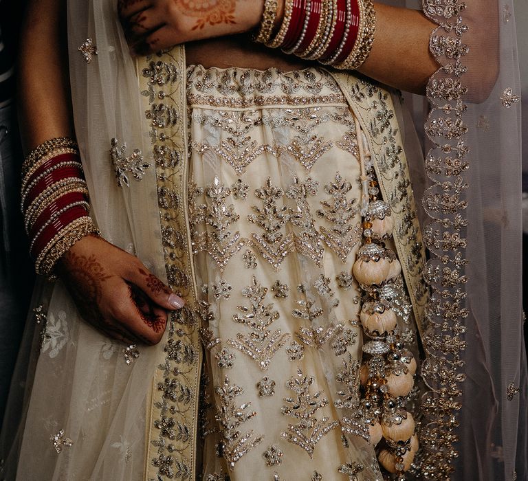 Bride wearing cream and gold two piece with red bangles up arms