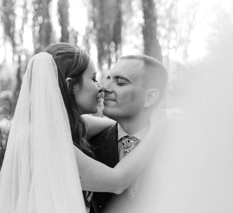 Black and white photography of newly wed couple hugging bride wears long veil 