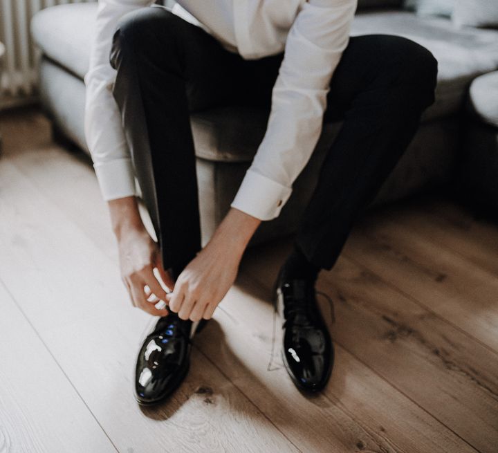 Groom in white shirt and bow tie ties his shoes whilst sitting down